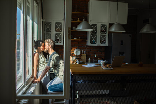 Couple kissing by the window in a sunlit kitchen