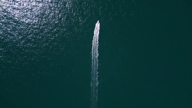 Aerial top down view of a motorboat speeding across deep blue ocean water