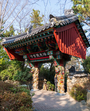 Busan, South Korea - 14 February 2026: View of Haedong Yonggungsa Temple entrance with traditional ornate wooden architecture, dragon-carved pillars, and lush surrounding trees.