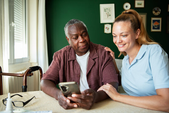 Caregiver helping senior man use smartphone at home