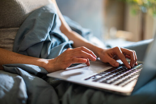 Person typing on laptop in bed at home