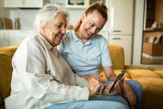 Caregiver helping senior woman use smartphone at home