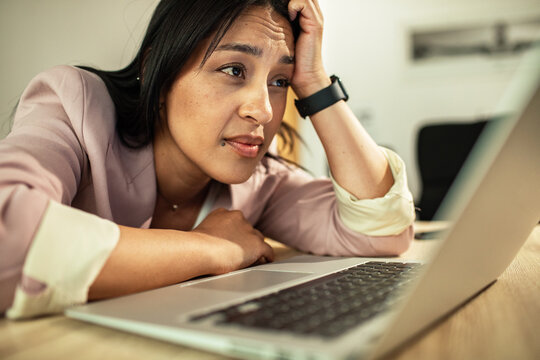 Tired businesswoman with hand on forehead at laptop
