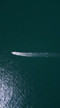 Aerial top down view of a motorboat speeding across deep blue ocean water