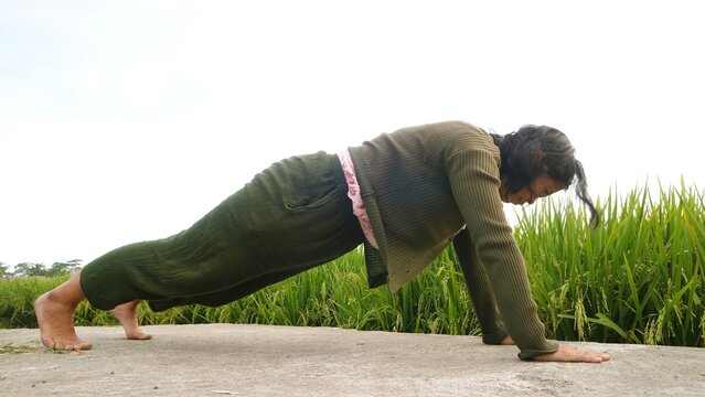 A woman performing a plank exercise outdoors in a green rural field setting.