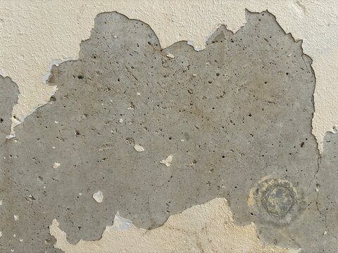 Large area of flaking paint layer exposing raw porous concrete wall background
