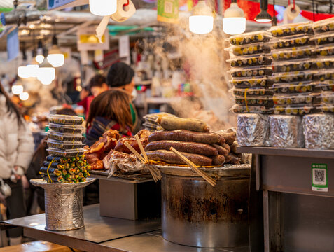 Busan, South Korea - 09 February 2026: View of a street food stall with steaming sausages and stacks of kimbap in a busy market.