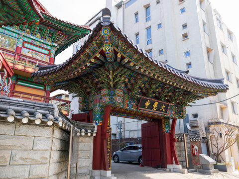 Busan, Busan, South Korea - 09 February 2026: View of the ornate traditional entrance gate of Dae Gak Sa Temple with intricate wooden brackets and tiled roof, set against a modern building.