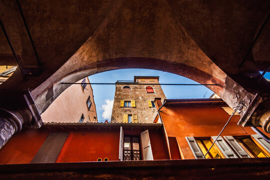 Bologna, Italy - 17 May 2018: View of a charming street in Bologna's historic city center, seen from beneath the city's characteristic arcades, with warm-toned buildings and a clear blue sky.