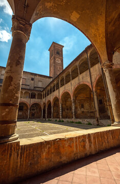 Bologna, Italy - 17 May 2018: View of the historic cloister with arched porticoes and a tall bell tower under a bright blue sky.