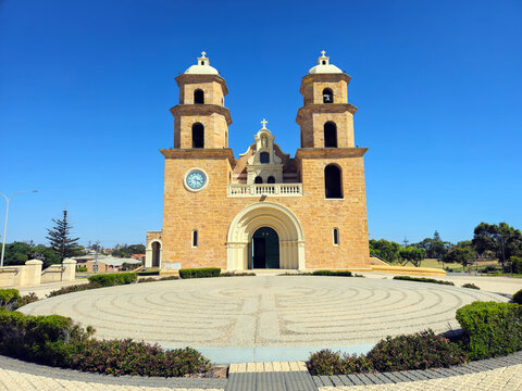 Geraldton, Western Australia, Australia - 29 December 2025: View of St Francis Xavier's Cathedral with its stone facade, twin towers, and a circular labyrinth in the foreground under a clear sky.
