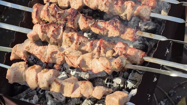 Appetizing and juicy meat skewers are grilling on metal skewers over hot mangal charcoal. Light smoke rises above the browned meat during outdoor picnic cooking