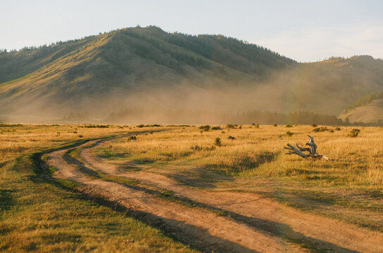 Sunlit dust rising from dirt road through golden mountain valley