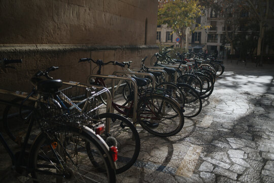 Palma de Mallorca, Spain - 04 January 2025: View of bicycles parked in a row along a stone wall in a historic urban square.