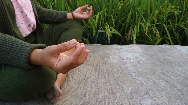 A person practicing meditation in a peaceful outdoor setting near green rice fields.