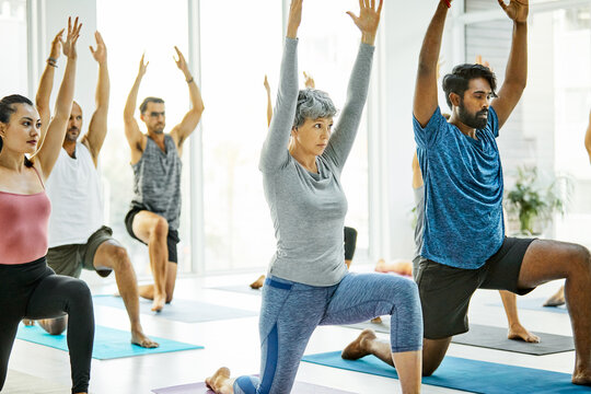 Stretching, people and yoga class with low lunge, functional mobility or arms up for core stability. Yogi, group and exercise in wellness studio with mindful movement, hip flexor relief and fitness