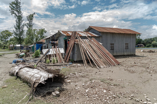 Noakhali, Bangladesh - 15 August 2026: View of simple wooden houses with scattered construction materials on sandy ground under a cloudy sky.