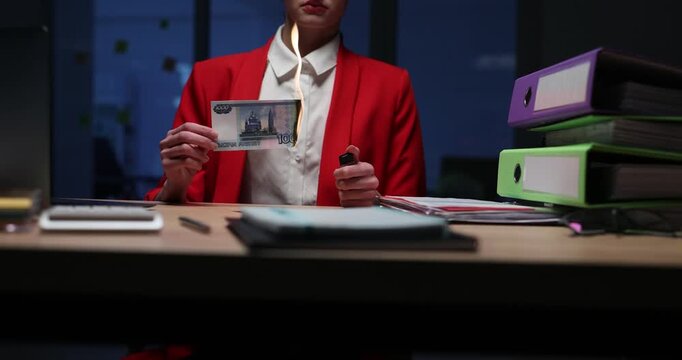 Office worker uses small lighter to ignite edge of enemy banknote. Businesswoman in formal office clothing works late in empty office. Slow motion