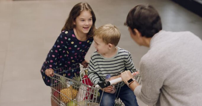 Supermarket, happy family and playing with trolley for shopping, fun retail errand and bonding. Above, mom or children with cart in store for weekly grocery run, playful moment or heathy relationship