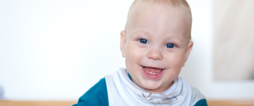 A cheerful young child with bright blue eyes beams with happiness while sitting indoors. Dressed in a teal outfit, this little one radiates pure joy in a cozy environment.