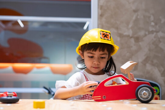 Young girl wearing a safety helmet and playing with a toy hammer at a pretend construction site, exploring creative roleplay, problem solving, imagination, practical skills, confidence, and learning.
