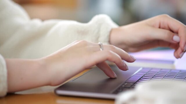 Close-up of woman typing on laptop. Hands with ring on finger. Soft lighting in background. Focused work in comfortable setting