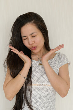 Young woman with long dark hair making silly face gesture in front of a plain wall