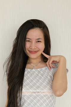 Woman with long dark hair smiling and making a gesture near her face against a plain background