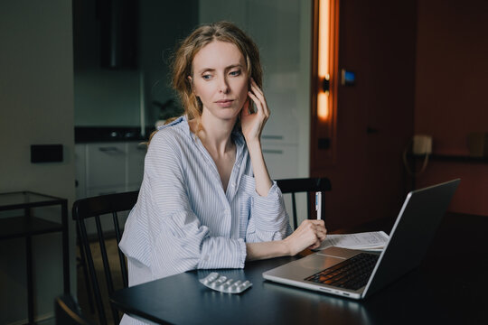 Woman with medicine uses a laptop at home while researching health symptoms online, illustrating AI-assisted self-diagnosis, self-treatment and digital healthcare concerns.