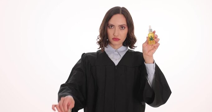 Lady judge holds pair of metallic handcuffs and bottle of hemp oil. Legal consequences associated with prohibited substances against white background