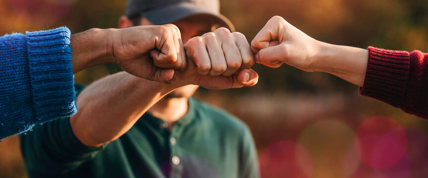 Diverse people joining hands for a firm fist bump gesture outdoors under soft golden sunlight rays