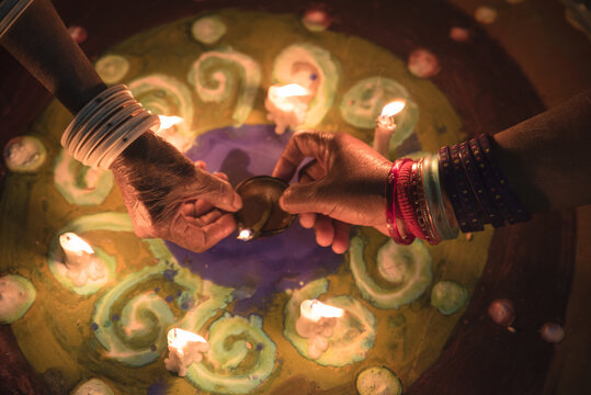 Rahim Yar Khan, Pakistan - 11 November 2015: View of hands adorned with bangles lighting a traditional diya lamp over a colorful rangoli pattern during the Diwali festival.
