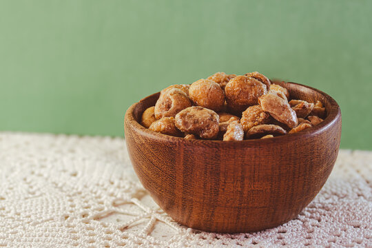 Glazed peanuts and almonds in a wooden bowl, a crunchy snack or sweet treat, a delicious mixture of nuts and caramel, isolated