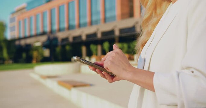 Close-up of woman hands scrolling through online pages on a smartphone outdoors on a city street