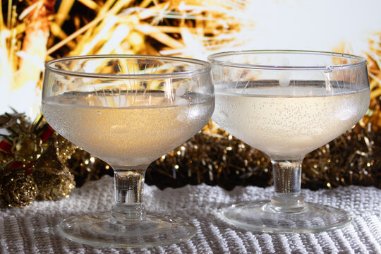 Two coupe glasses filling with sparkling champagne amid golden Christmas decorations and blurred lights, creating a warm, festive, romantic holiday toast atmosphere