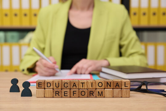 In a bright office filled with organized files, a person in a green blazer writes notes, emphasizing the importance of educational reform.