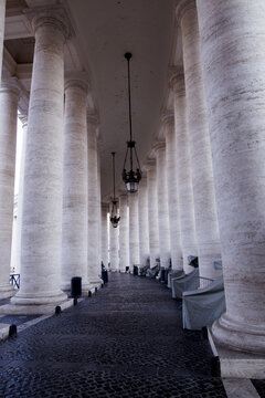 Vatican City, Vatican City - 03 October 2022: View of the massive stone columns of the Bernini colonnade in St. Peter's Square with hanging lanterns and cobblestone ground.