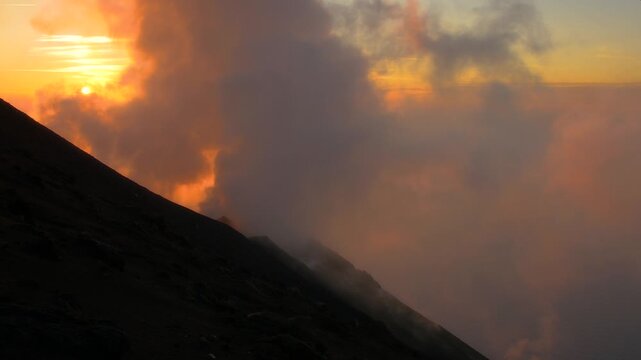 View of the volcanic slope of Stromboli volcano emitting smoke during a vibrant golden hour sunset in Stromboli, Sicily, Italy.