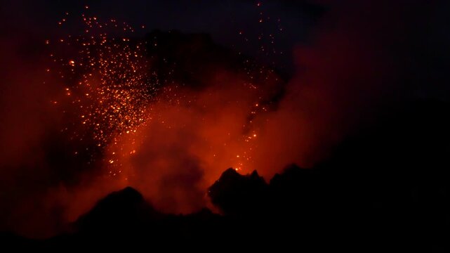 View of Stromboli volcano erupting at night with glowing lava and dark smoke plumes rising into the night sky in Stromboli, Sicily, Italy.