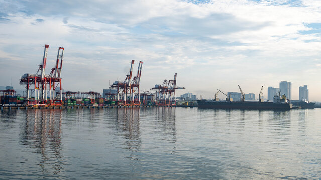 View of the Cebu Port Authority with container cranes, a cargo ship docked at the pier, and the city skyline under a soft morning sky in Cebu City, Central Visayas, Philippines.