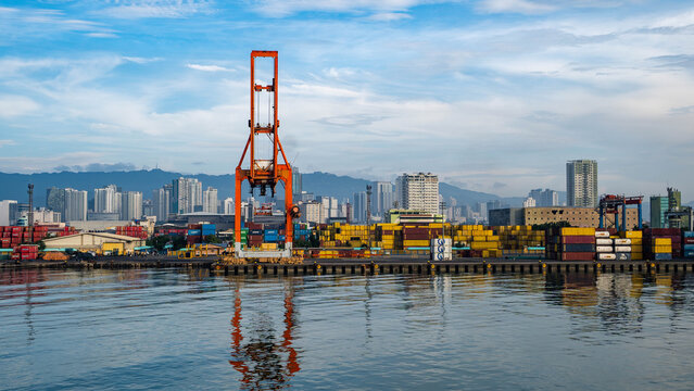 View of the Cebu Port Authority with colorful shipping containers, a large orange crane, and the city skyline in the background in Cebu City, Central Visayas, Philippines.