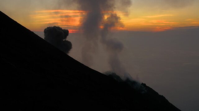 View of Stromboli volcano emitting smoke against a vibrant sunset sky in Stromboli, Sicily, Italy.