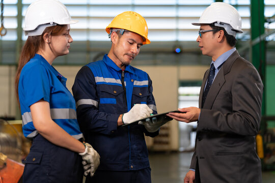 A factory technician presents a clipboard during discussion with a manager and colleague, showing industrial coaching, operational review, teamwork, and maintenance coordination.
