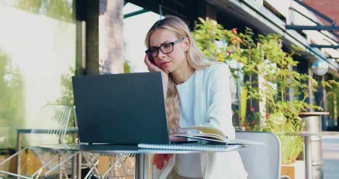 Disappointed Caucasian woman looking at laptop screen while sitting at a table outdoors