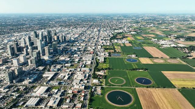 Expanding urban skyline meets rural agricultural land in this motion drone footage showing contrast between development and nature aerial view