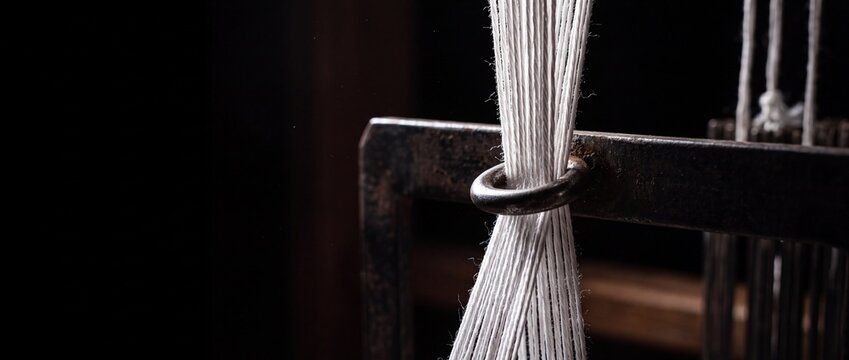 Close up of white threads on old metal loom with dark background weaving fabric.