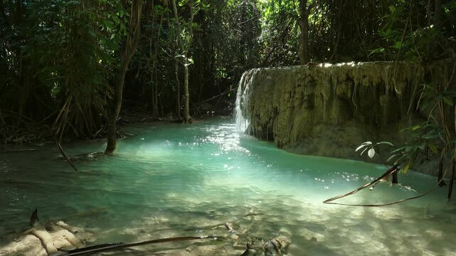 View of the turquoise water of Erawan Falls surrounded by lush jungle and limestone rock formations in Tha Kradan, Kanchanaburi, Thailand.