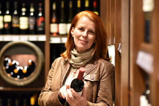 older woman buys a bottle of wine in a store