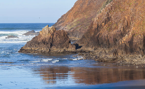 Beautiful wide view of sharp volcanic rocks on an ocean beach with a reflection at sunrise