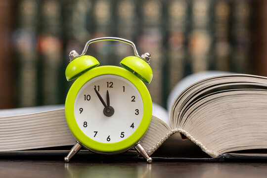 A clock and an open book against the background of a bookshelf.